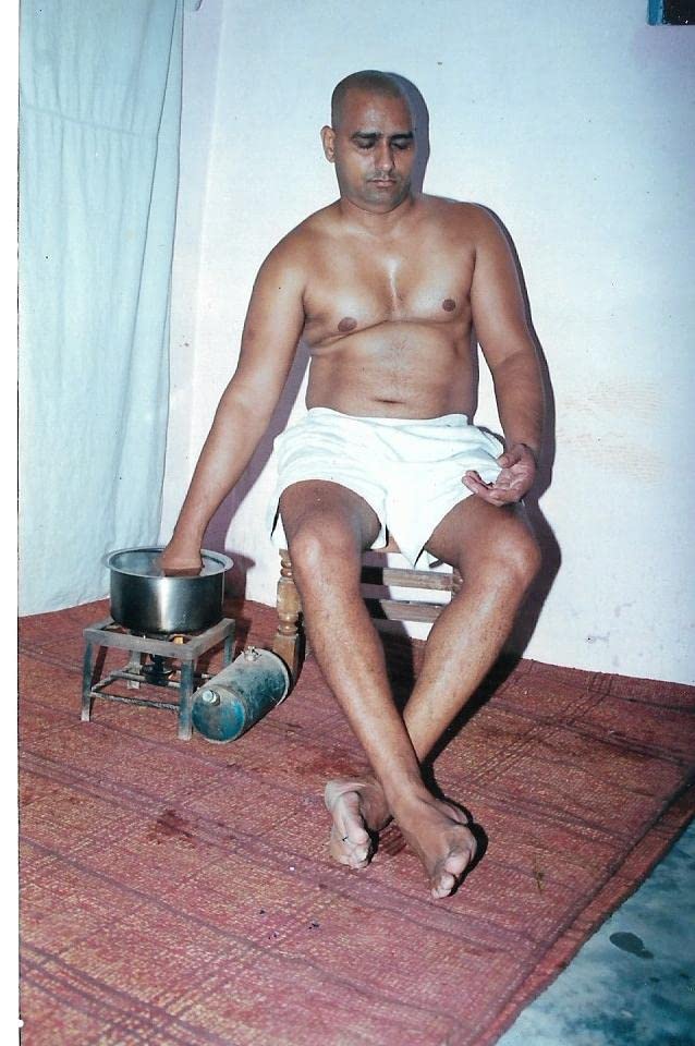 Man sitting on a chair performing a demonstration with his hand in a pot over a gas burner, showcasing a hypnotism or yogic practice.